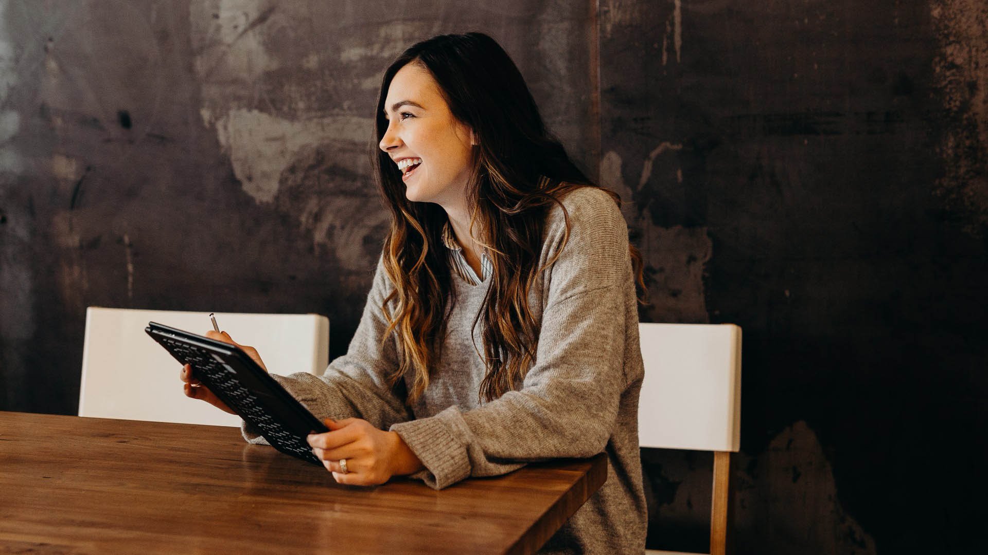 Woman sitting by a desk smiling with her tablet