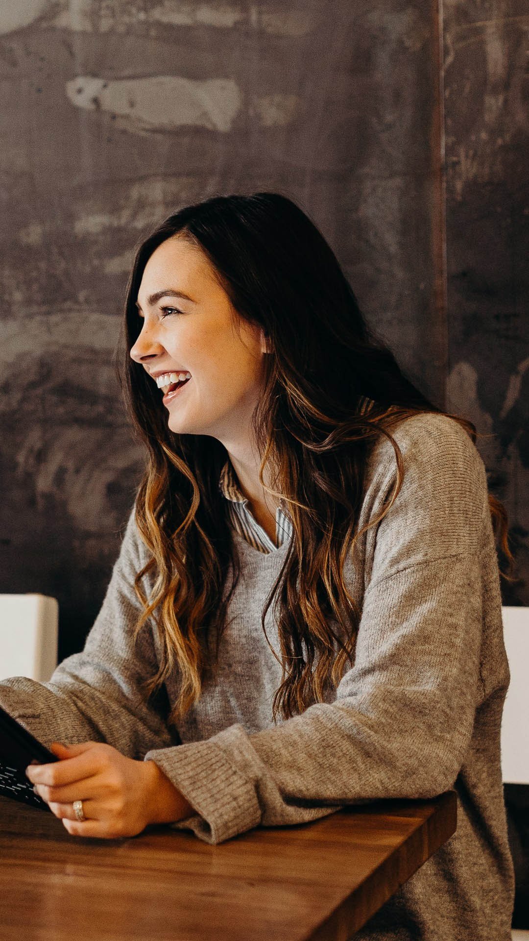 Woman sitting by a desk smiling with her tablet